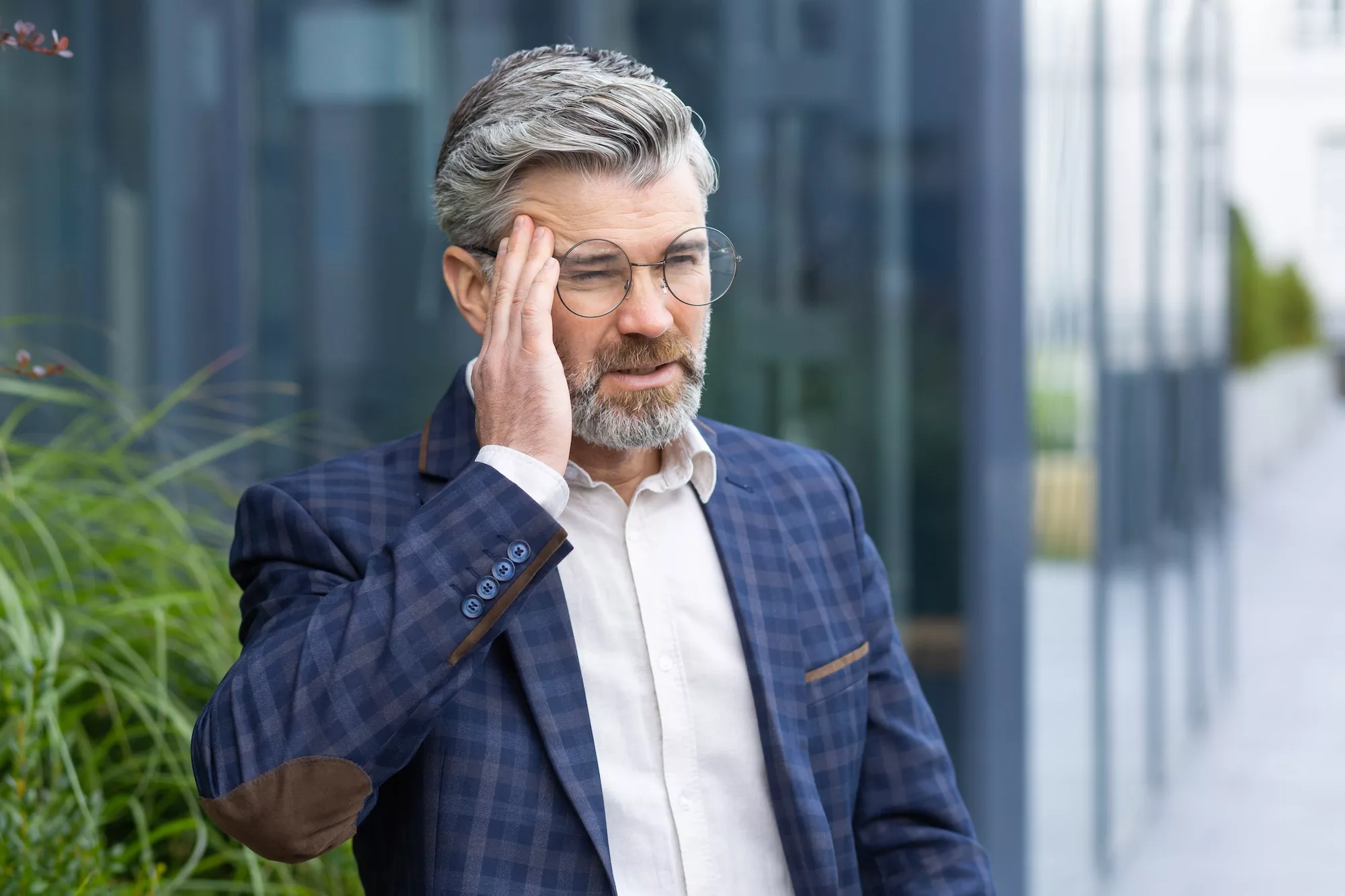 Sick and sad mature businessman outdoors sitting on bench on office building background, senior